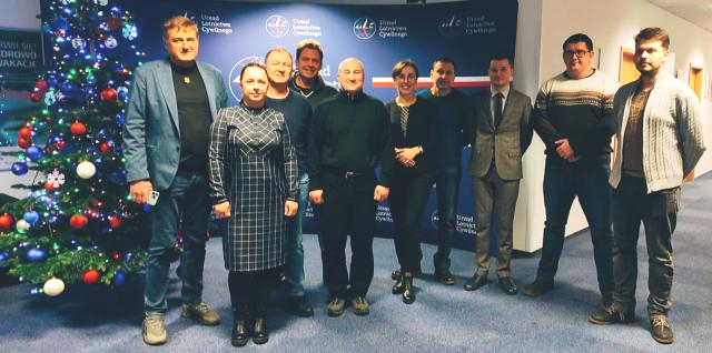 Grupa osób na tle ścianki z nazwą Urzędu Lotnictwa Cywilnego. Z lewej strony stoi świąteczna choinka.